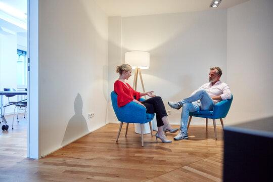 Mature man and young woman sitting in armchairs talking