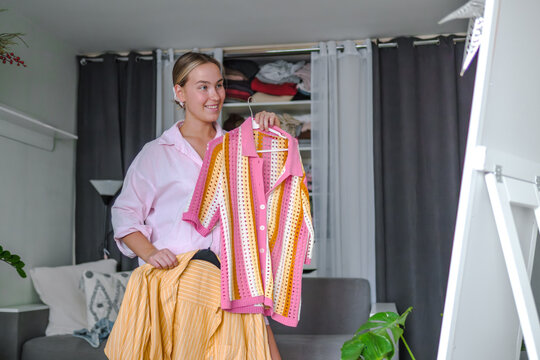 Woman chooses secondhand fashion clothing in her bedroom
