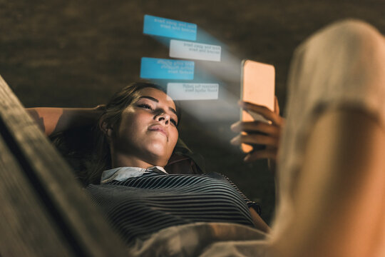 Young woman lying on bench at night with text emerging from smartphone 