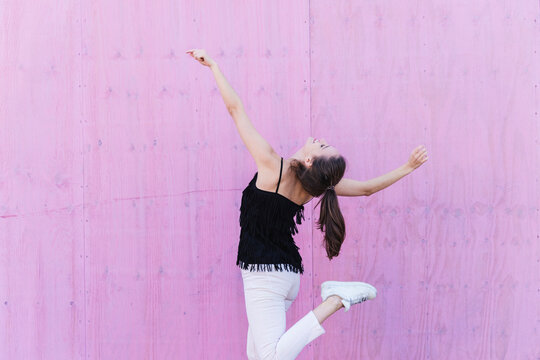 Happy young woman moving in front of pink wall