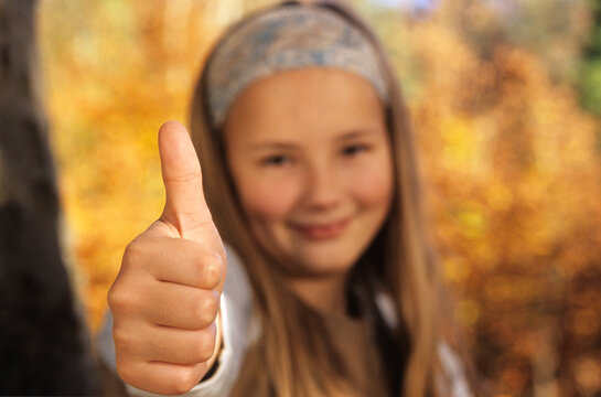 Girl (11-14) giving 'thumbs up' outdoors, focus on thumb