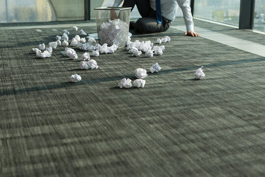 Businessman sitting on office floor surrounded by crumpled paper