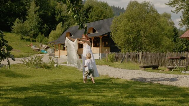 A woman and her little boy have fun playing outside an old house in Bucovina. They enjoy a sunny day and share laughter while spending time together.