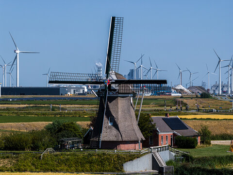 Eemshaven, Netherlands - 13 August 2026: Aerial view of a traditional Dutch windmill in a flat landscape with modern industrial wind turbines in the background under a clear sky.