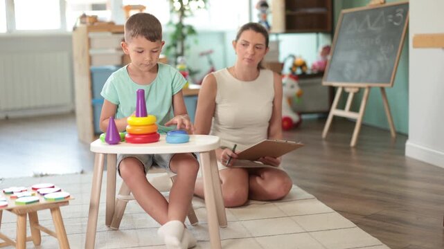 Boy sits at table and builds pyramid out of plastic toy cups. Childs behavior as marker of mental and mental health and development. Developing and maintaining skills for children with special needs