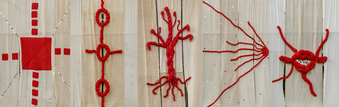 a textile installation meticulously sculpted from braided and unraveled red fibers against a neutral fabric background