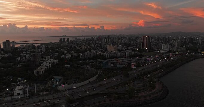 Beautiful sunset view of Mumbai, Maharashtra, with a dramatic orange sky illuminating the city skyline and calm waterfront. The glowing clouds, shimmering water, and striking evening cityscape.