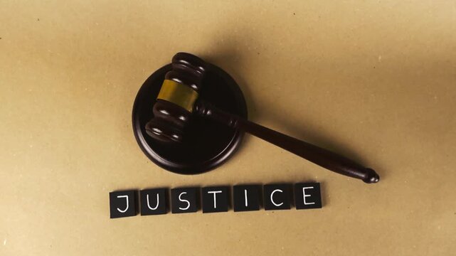 Wooden judge gavel with the word justice spelled out on a rustic paper background representing law, legal system, court proceedings, fairness, and the concept of judgment in a courtroom