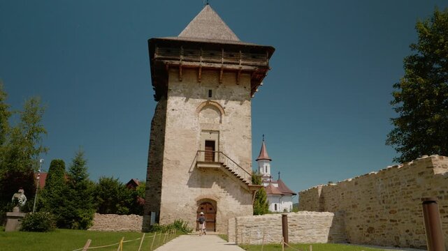 A mother and child stroll past the old walls and tower at Humor Monastery in Bukovina. They admire the ancient paintings on the site during their visit.