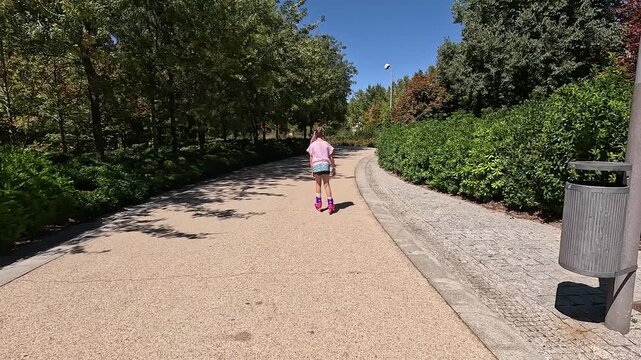 Behind a preteen girl skating on a paved pedestrian path in a forest next to the river in the city of Madrid, Spain