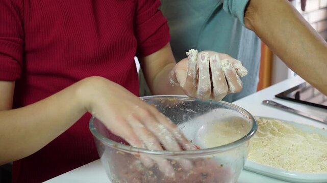 Child hands shaping homemade raw beef meatballs in a glass bowl on the kitchen counter
