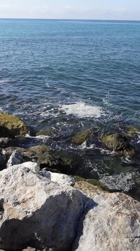 Vertical shot of contaminated coastline with a scum of dirt foam on the water surface of the polluted ocean crashing against rocky seashore
