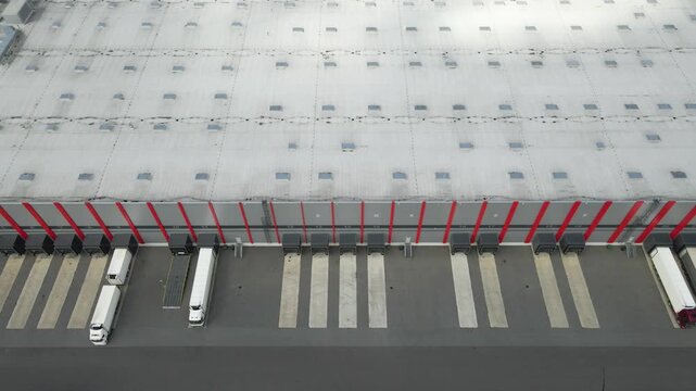 High aerial view showing semi trucks maneuvering and backing into the loading bays of a large industrial warehouse, a modern distribution center for logistics and supply chain operations
