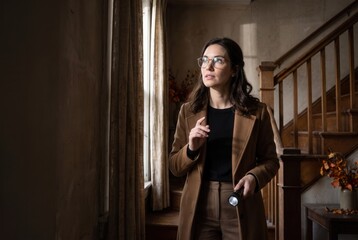 Obraz premium Woman holding a flashlight, cautiously exploring a dark, abandoned house interior