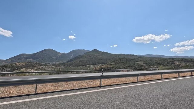 Mountains with olive groves in rows seen from a vehicle driving on a highway in Jaen, Andalusia, Spain
