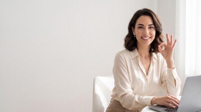 Smiling businesswoman working on laptop, showing okay gesture