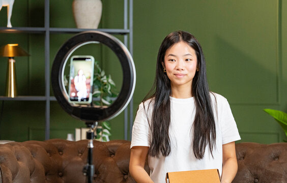 Young woman recording content with smartphone and ring light, holding a cardboard box
