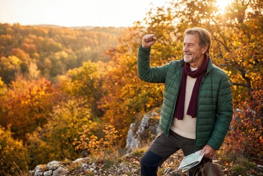 Smiling older man reaching mountain peak in colorful autumn forest, holding map