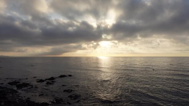Time-lapse of stunning horizon line on the sea with sun between clouds at dawn or dusk. Sky and ocean waves moving fast

