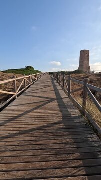 Vertical shot capturing the journey along a wooden footpath towards the ancient Thieves Tower, built in the 1500s, within the Artola Dunes of Cabopino, Marbella (Malaga, Andalusia, Spain, Europe).
