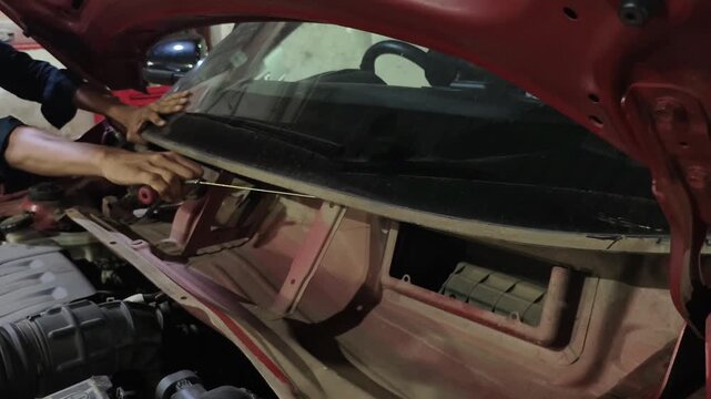 Mechanic removes damaged front windshield from car at automotive repair garage. Footage shows windshield replacement and auto glass repair process, highlighting vehicle maintenance