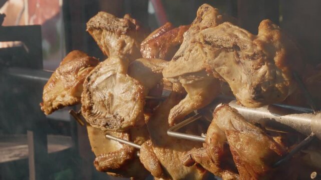 Chickens spin slowly on a grill, cooking over an open flame at a busy street food festival in Bukovina. The smell fills the air as people gather around.