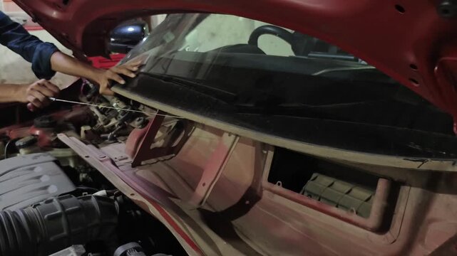 Mechanic removes damaged front windshield from car at automotive repair garage. Footage shows windshield replacement and auto glass repair process, highlighting vehicle maintenance