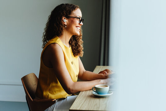 Curly-haired african-american woman smiling at desk during remote work on laptop