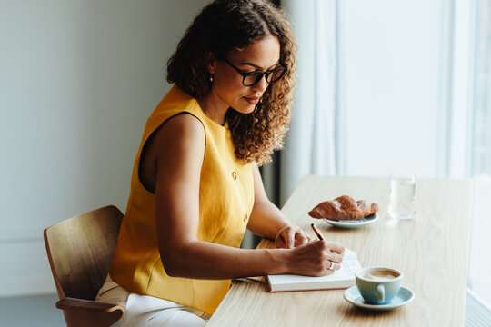 Focused woman writing in a journal with coffee and pastry