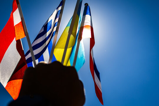 Sunlight crowns a fan of small flags lifted by a strong hand. Blue and yellow tones shine among other patterns. The composition honors resilience cross border friendship and peaceful aims
