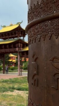 Verkhnyaya Ivolga, Russia - July 23, 2026: Ornate Tibetan prayer wheel stands prominently with traditional pagoda structures and greenery visible in the serene landscape