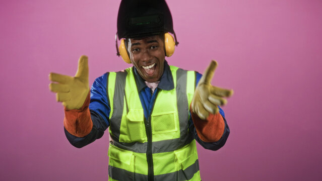 Man wearing welding helmet and high visibility vest gives double thumbs up with gloved hands in studio; work pride.