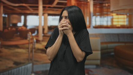 Fototapeta premium Woman covering mouth with hands laughing in airport lounge, shoulders raised and eyes squinting; amusement surprise.