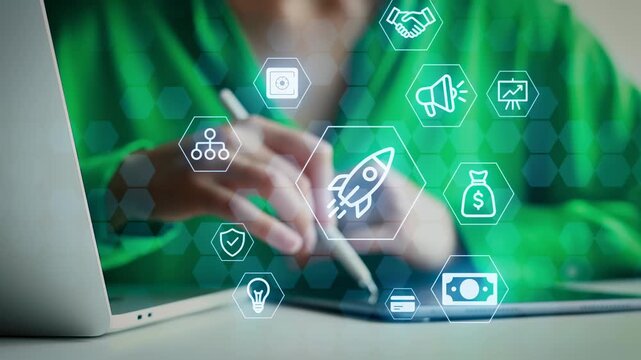A person is sitting at a table with a laptop open. They are working on a digital marketing project. Various icons related to marketing are displayed around their hands.