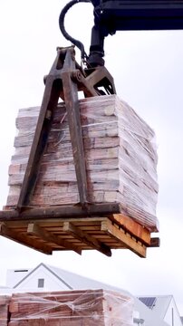 Loader crane use brick grab to lift brick pallet off transport truck. Vertical