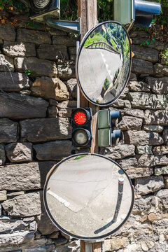 Convex traffic mirrors and red signal light on stone wall in historic village street