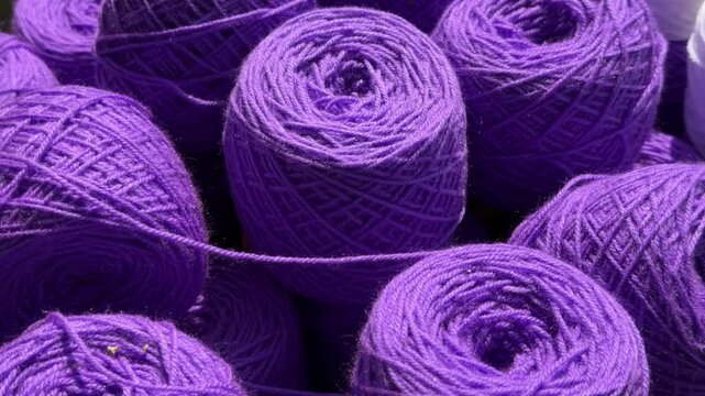 Close-up of multiple rolls of purple yarn prepared for knitting, crochet, tufting and other textile crafts.