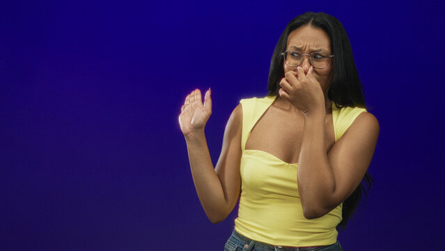 Woman pinching nose with hand and grimacing, other hand raised in a stop gesture in a studio; disgust avoidance.