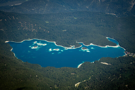 Aerial View of Turquoise Lake Eibsee Surrounded by Alpine Forest Below Zugspitze Mountain - Germany