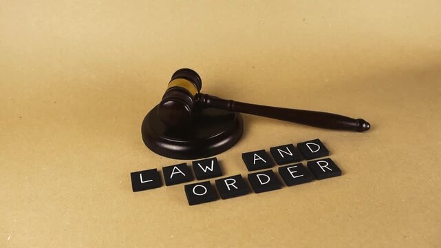 Wooden judge gavel with a sound block laying next to letters spelling law and order on a brown background, representing the concept of legality, justice, auction, and court rulings