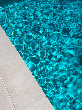 Water ripples, abstract blue color pool water, pool tiles border, edge, caustic effect, background of beautiful blue clear transparent water surface with waves and reflections. Top view, vertical 