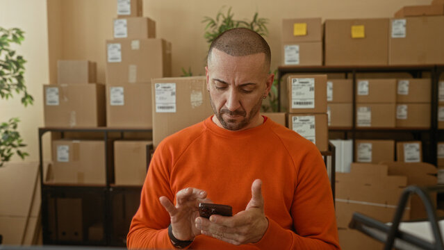Man hands tapping smartphone amid stacked cardboard boxes in a building parcel office; small business focus.