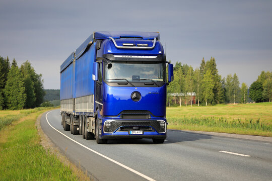 Blue Mercedes-Benz Actros L GigaSpace ProCabin semi-truck hauling double tarp top trailer on the road under dark sky. Copy space.
