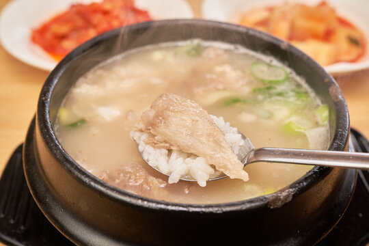 Close up of traditional Asian beef tendon soup in a black pot. A spoon holds rice gelatinous meat and diced radish kimchi. Highlights authentic gastronomy perfect for restaurant marketing.