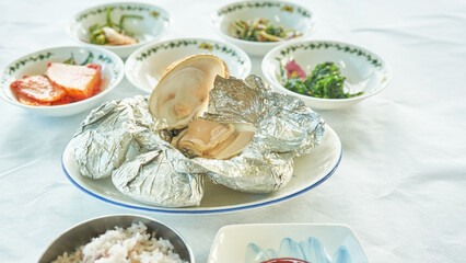 A close up macro of traditional Asian seafood dining featuring fresh hard clams and mixed grain rice. Foil wrapped steamed shells and vibrant side dishes highlight authentic regional coastal gastronom © 진영김