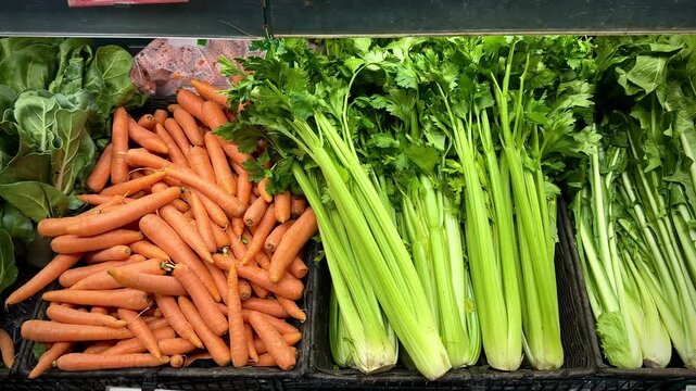Fresh green celery stalks arranged neatly in a market display, showcasing vibrant leaves and crisp texture, with other vegetables partially visible in the background