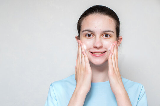 A smiling beautiful girl's face in acne uses a foaming cleanser. Teenage skin care concept, copy space