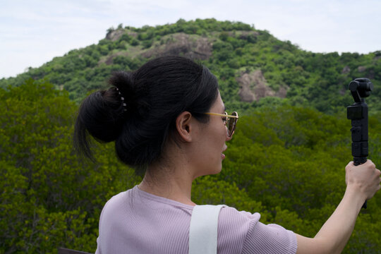 Woman filming a mountain and mangrove forest view with a gimbal camera