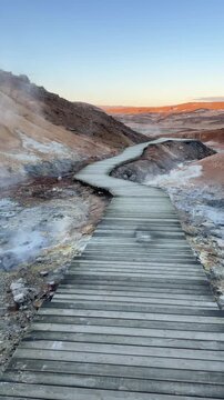 Iceland. Colorful geothermal landscape with steaming blue water and mineral-rich earth, showcasing a series of rocky formations and wooden walkways in a natural hot spring area