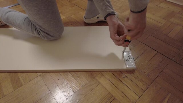 Homeowner examines roller operation on polished parquet flooring carefully. Closeup of homeowner checking roller mechanism and smooth sliding motion on wooden floor